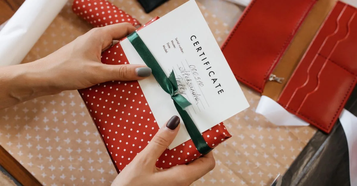 Gros plan de mains tenant un chèque-cadeau enveloppé dans du papier à pois rouges et un ruban vert.