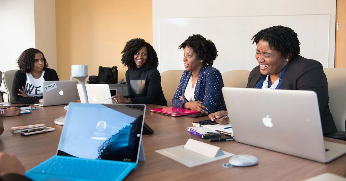 Groupe de femmes participant à une réunion collaborative autour d'une table de bureau avec des ordinateurs portables.