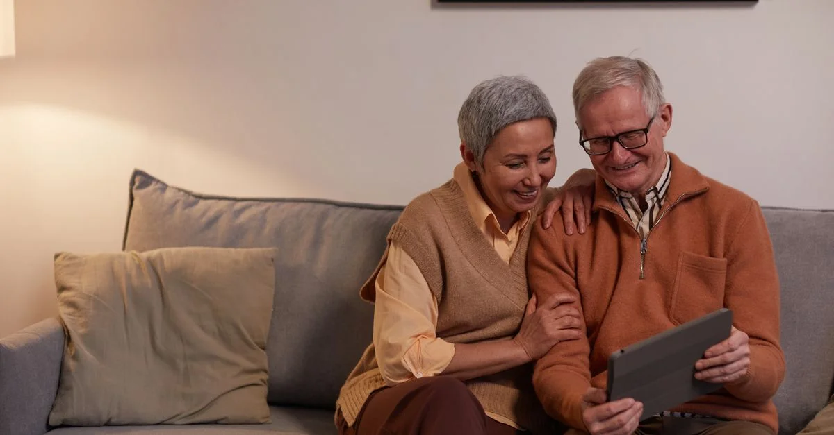 Un couple senior souriant et utilisant une tablette dans leur salon confortable.