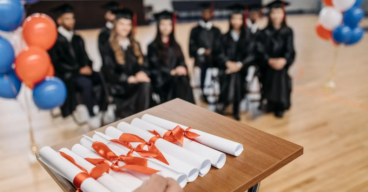 Cérémonie de remise des diplômes avec des étudiants assis, des diplômes et des ballons festifs.