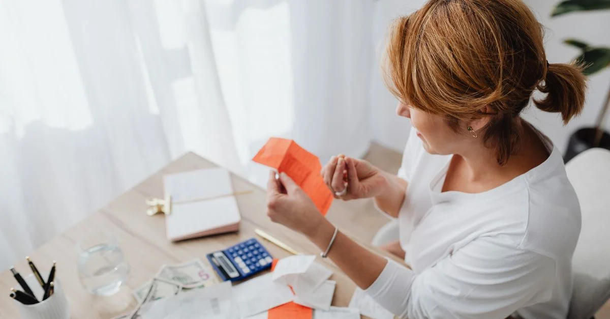 Une femme organise ses finances avec des factures et des reçus sur un bureau de bureau à domicile en utilisant une calculatrice et un ordinateur portable.