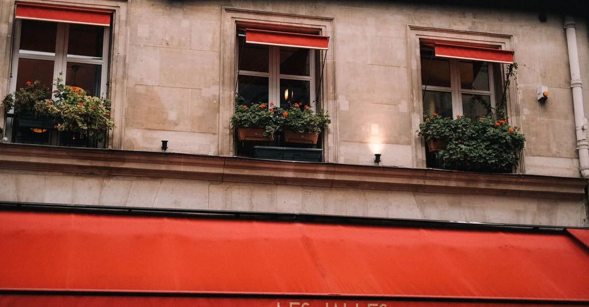 Une façade pittoresque de bâtiment parisien avec des auvents rouges et des jardinières fleuries dans un cadre urbain.