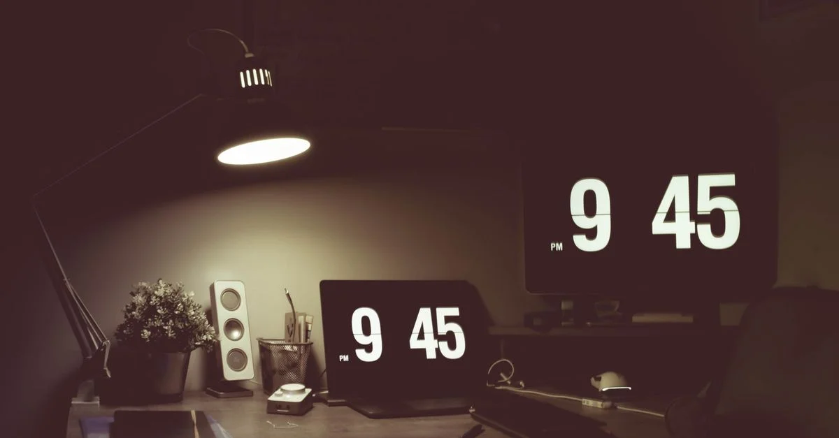Un espace de travail confortable comprenant des horloges numériques, une lampe de bureau et des appareils modernes dans une faible luminosité.