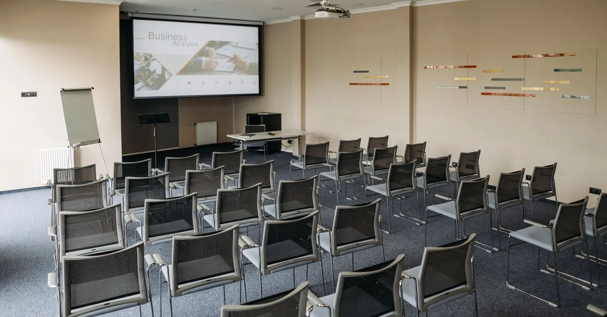 Salle de conférence vide avec des rangées de chaises, écran et tableau blanc.