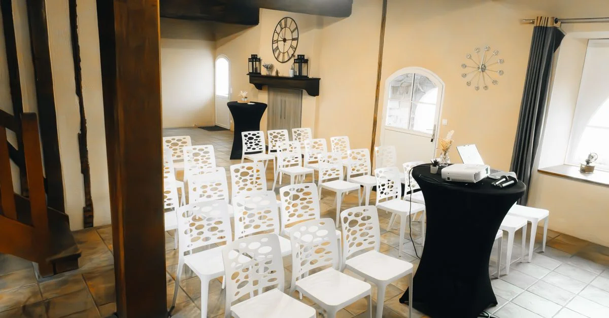 Salle de conférence spacieuse avec chaises blanches élégantes et décoration moderne, idéale pour les séminaires.