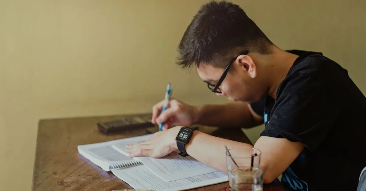 Un jeune homme se concentre sur ses études à son bureau, prenant des notes à l'intérieur.