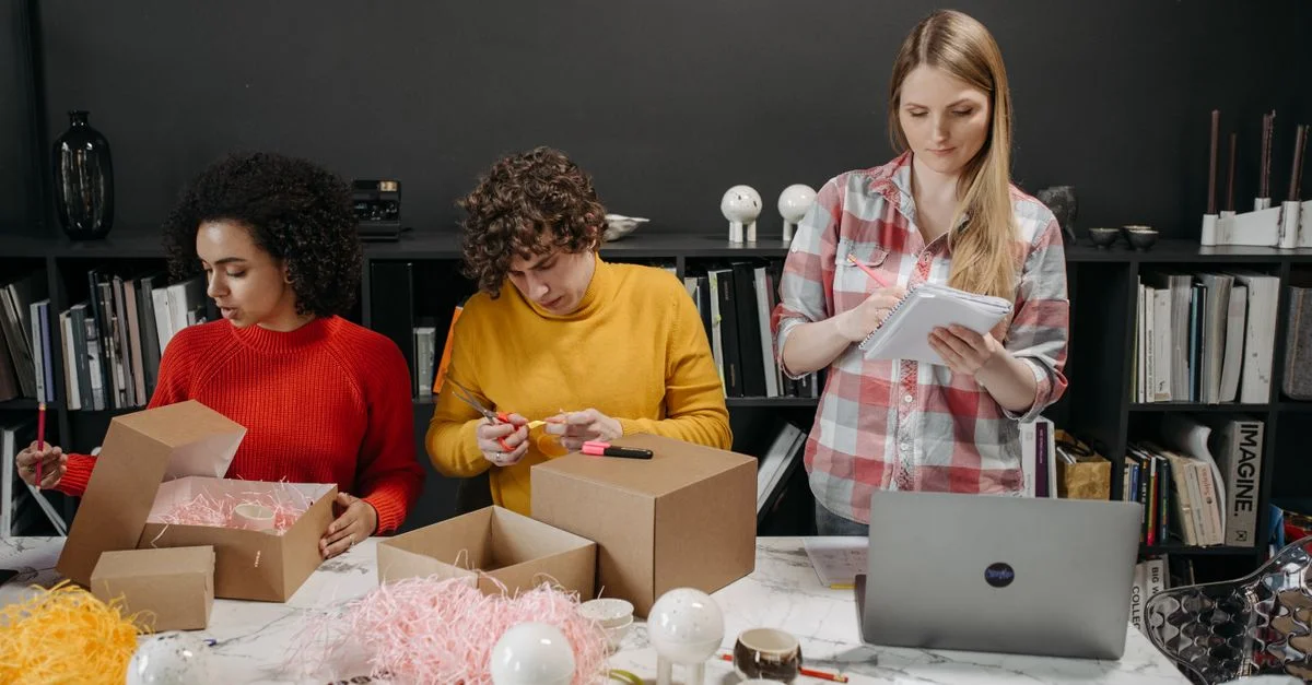 Équipe diversifiée travaillant ensemble, préparant des colis dans un environnement de bureau créatif.