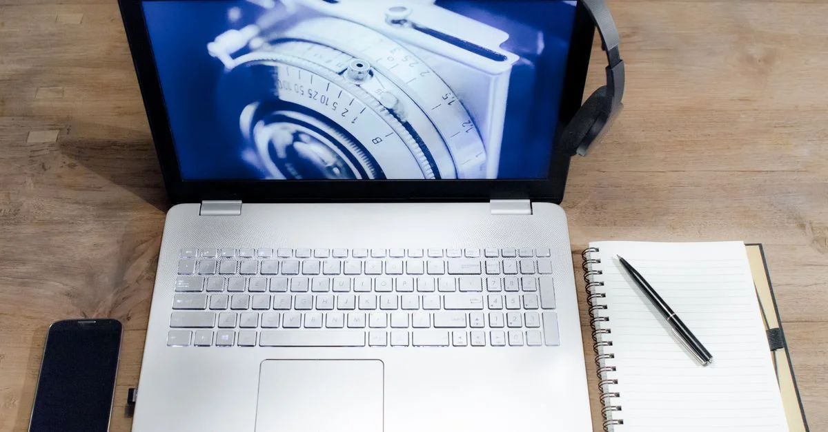 Vue de dessus d'un espace de travail moderne avec un ordinateur portable, un smartphone, des écouteurs et un carnet sur un bureau en bois.