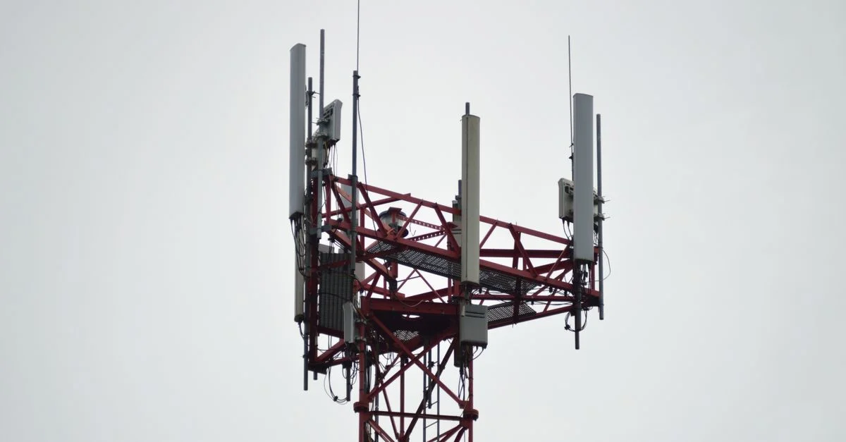 Une tour de communication rouge avec des antennes se dresse contre un ciel gris.