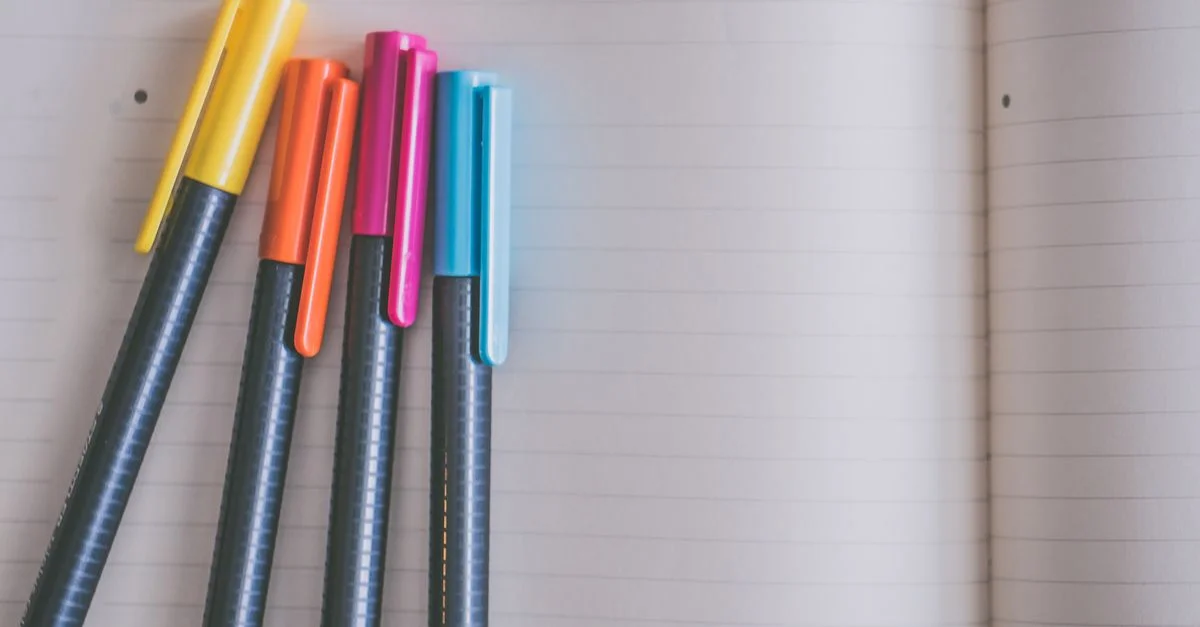 Une collection de stylos colorés reposant sur un carnet à lignes ouvert, créant un espace de travail vibrant et accueillant.