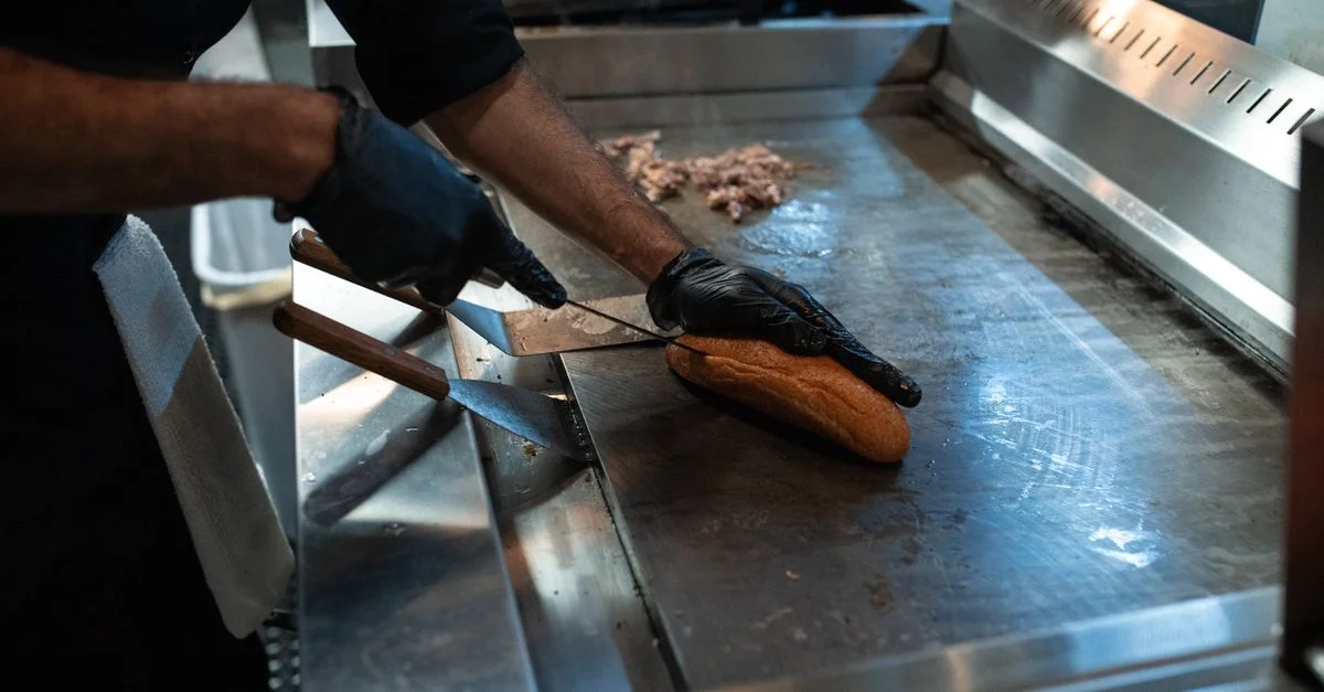 Chef tranchant du pain sur le gril, préparant un sandwich dans un cadre de cuisine professionnel.