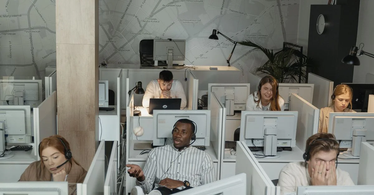 Un groupe d'employés de centre d'appels divers travaillant sur des ordinateurs et portant des casques dans des cubicles.