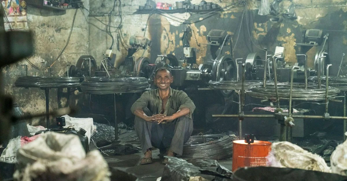 Un travailleur est assis heureux dans une usine rustique entouré de machines et de fils.