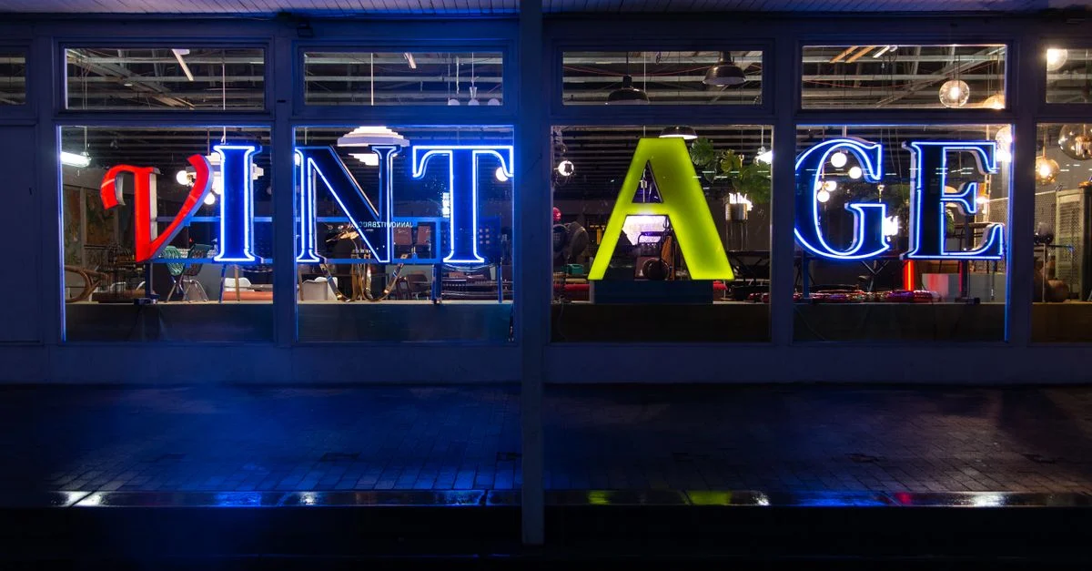 Une enseigne lumineuse « VINTAGE » au néon, illuminée dans la vitrine d'un magasin, crée une ambiance nostalgique.