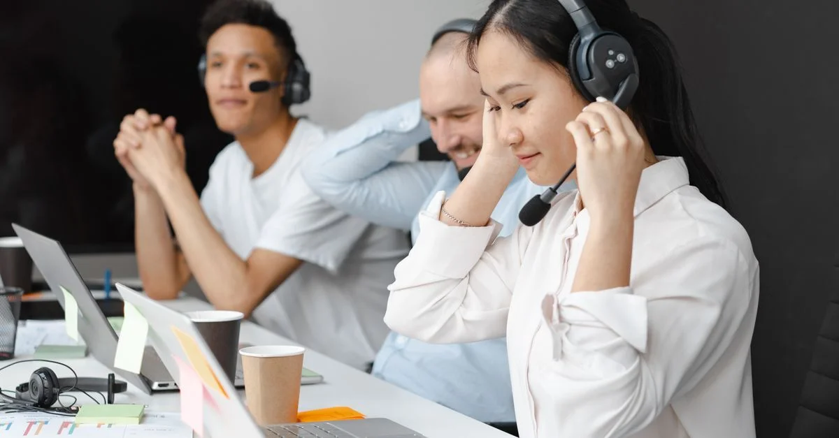 Équipe diversifiée d'agents de centre d'appels utilisant des ordinateurs portables et des casques dans un cadre de bureau moderne.
