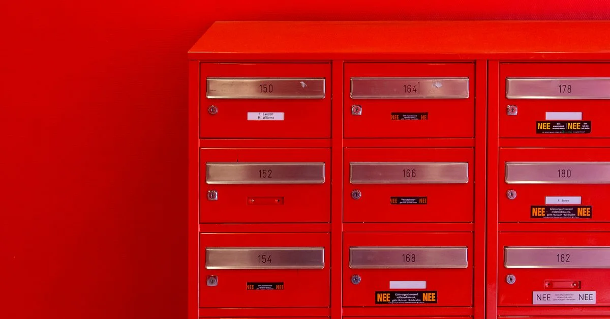 Une rangée de boîtes aux lettres rouges élégantes avec des panneaux numérotés métalliques et des serrures sur un fond rouge.