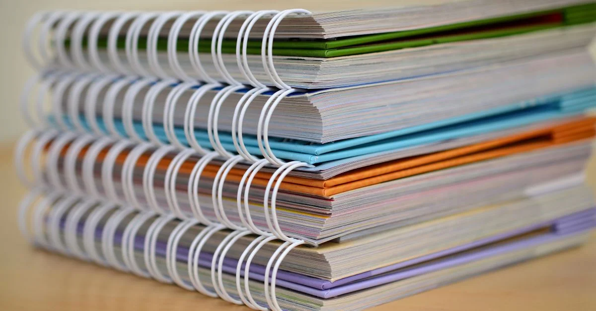 Une pile colorée de cahiers à spirale soigneusement disposée sur un bureau en bois. Idéal pour des thèmes éducatifs.