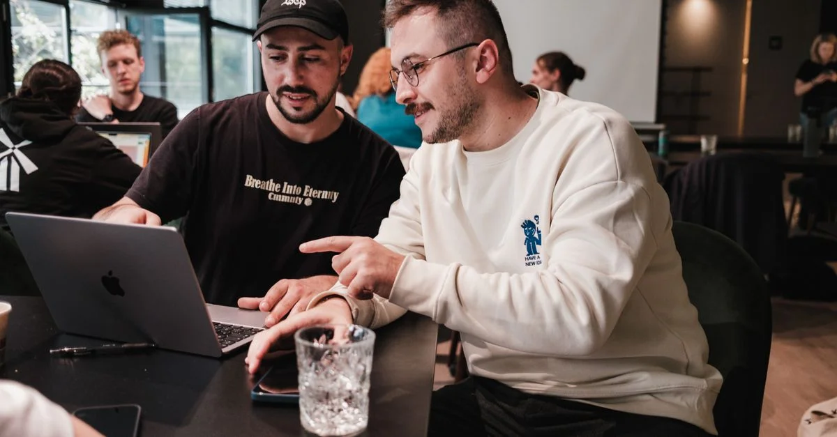 Deux collègues collaborent sur un ordinateur portable dans un café moderne, favorisant le travail d'équipe.
