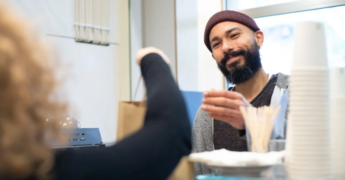 Un barista souriant remet un sac en papier à un client dans un café accueillant, mettant en avant un service client chaleureux.