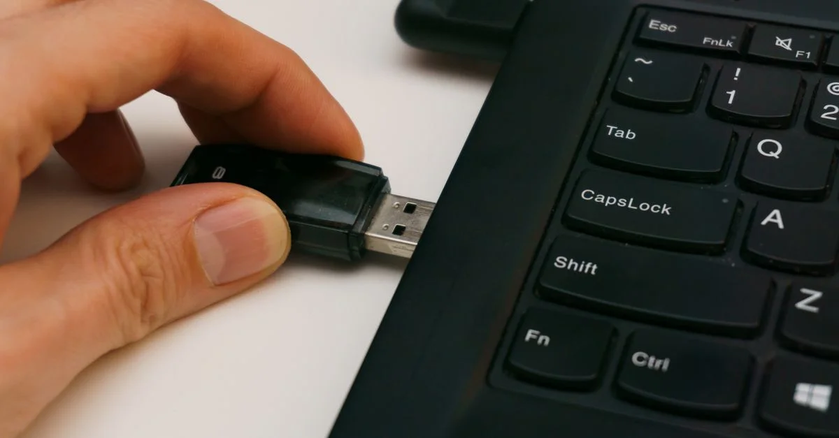 Gros plan d'une clé USB insérée dans un port USB d'un ordinateur portable sur une surface blanche.