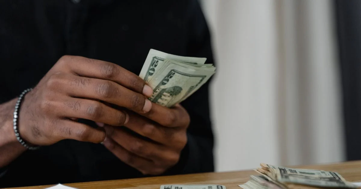 Adulte comptant des billets de dollar à un bureau, concentré sur la gestion de l'argent et les finances.