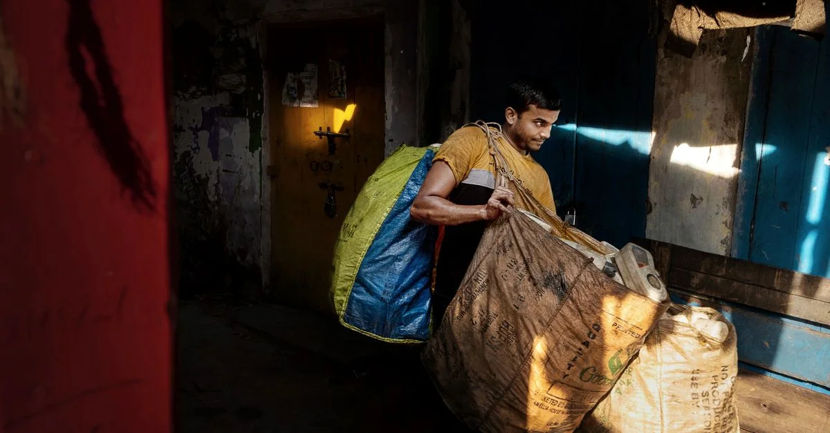 Un homme portant des sacs lourds dans un environnement intérieur faiblement éclairé, mettant en avant le travail acharné.