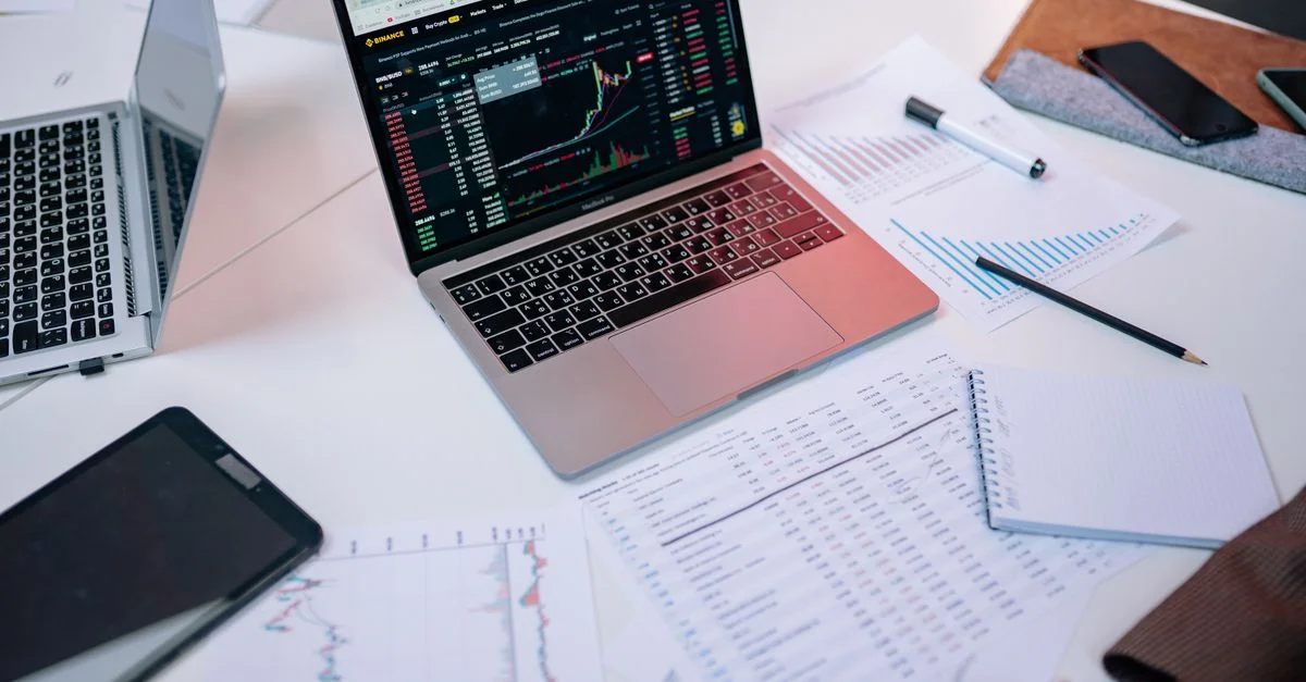 Ordinateurs portables sur un bureau affichant des graphiques boursiers et des documents financiers.