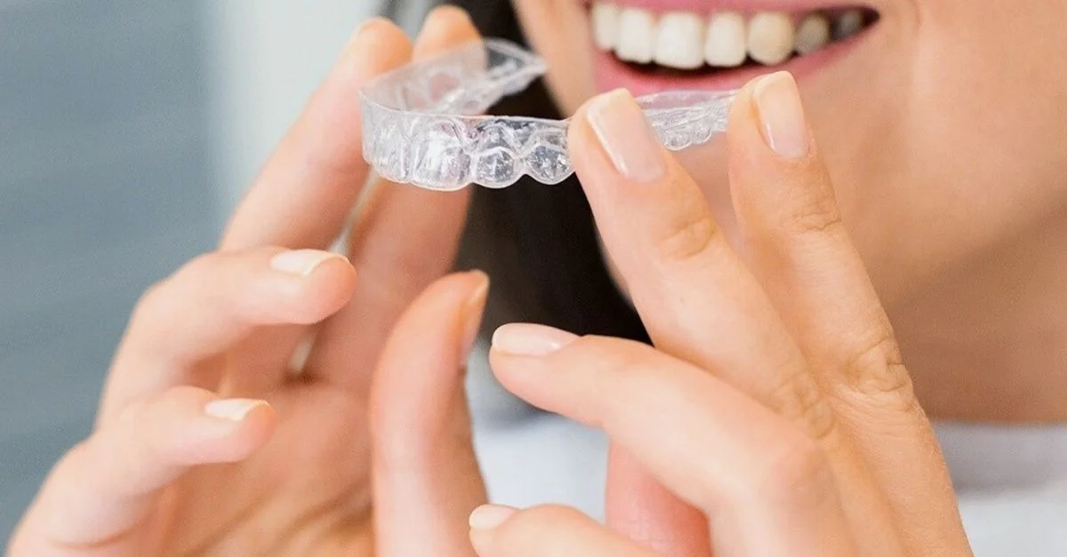 Gros plan sur une femme tenant un aligneur dentaire transparent, mettant en avant la santé dentaire et un sourire éclatant.