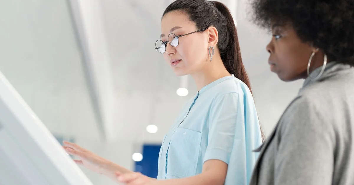 Deux femmes diverses utilisant un écran interactif dans un cadre intérieur moderne.
