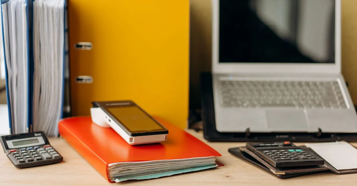 Bureau avec ordinateur portable, documents et calculatrices, idéal pour la productivité professionnelle.