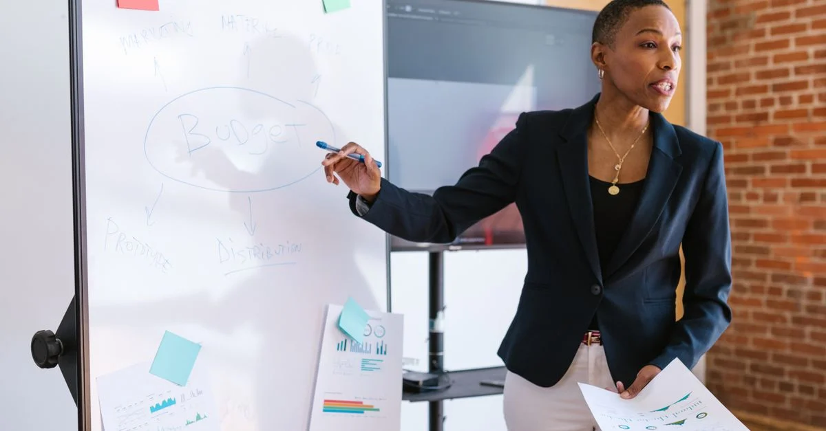 Femme d'affaires professionnelle expliquant la stratégie budgétaire sur un tableau blanc lors d'une réunion.