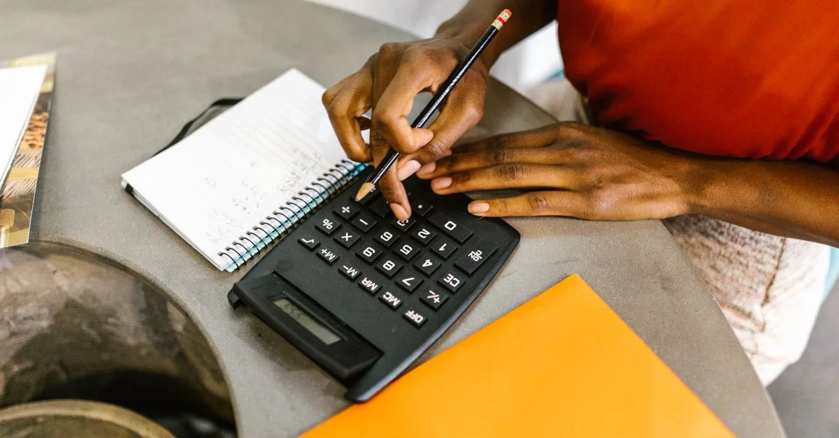 Une femme afro-américaine utilisant une calculatrice et un bloc-notes pour établir un budget.