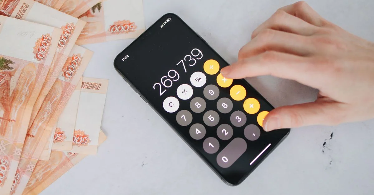 Personne utilisant une calculatrice sur smartphone avec des roubles russes sur une table, représentant la planification financière.