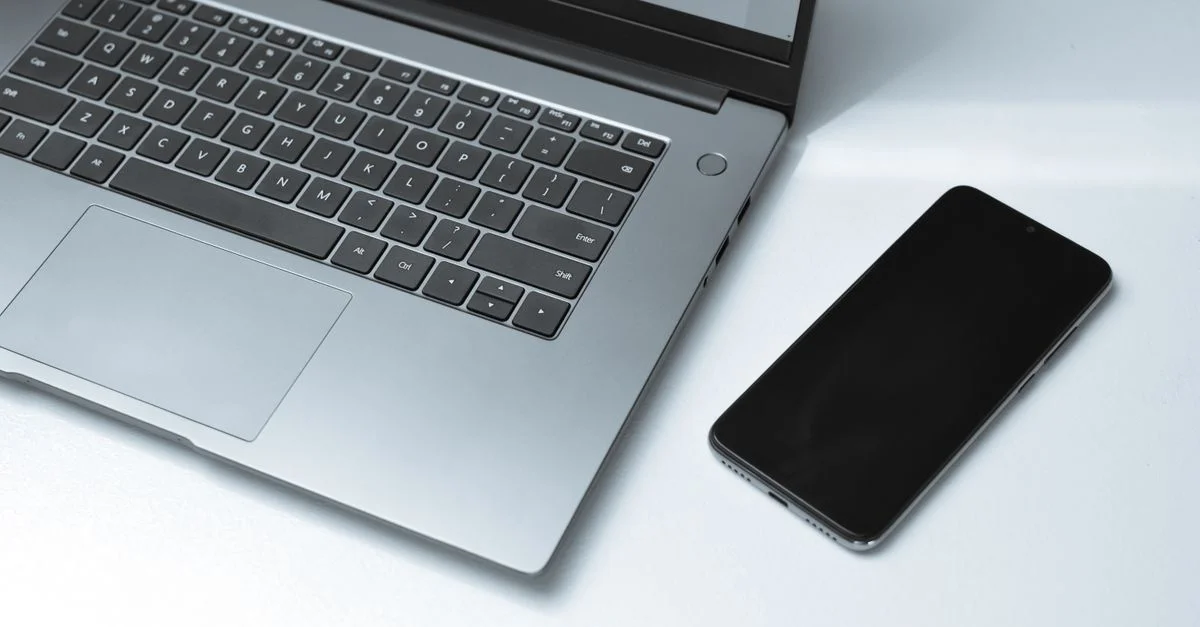 Un ordinateur portable argenté élégant et un smartphone sur un bureau blanc lumineux en plein jour.