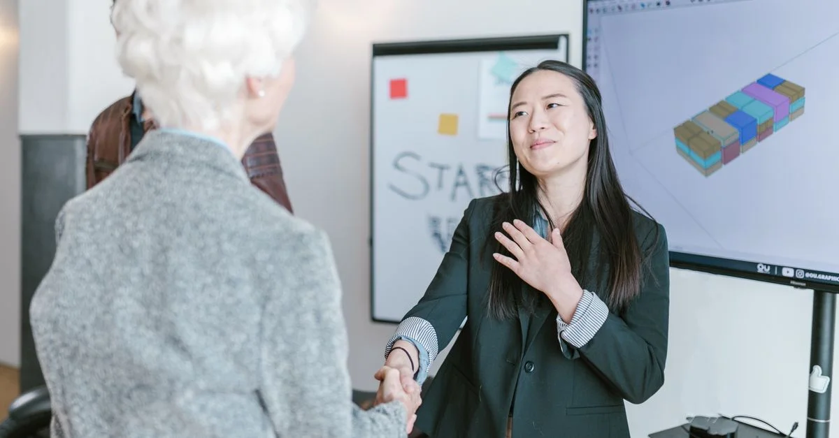 Des femmes professionnelles se serrant la main dans un bureau corporate, symbolisant un accord commercial réussi.