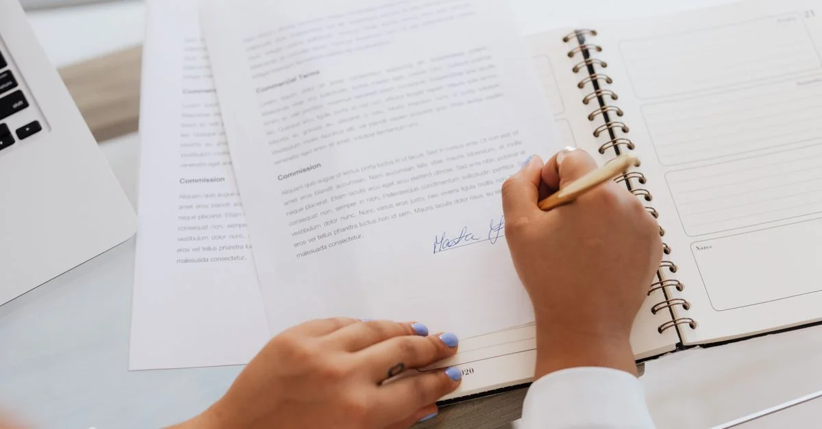 Gros plan des mains signant un contrat sur un bureau avec des fournitures de bureau, symbolisant des accords légaux.