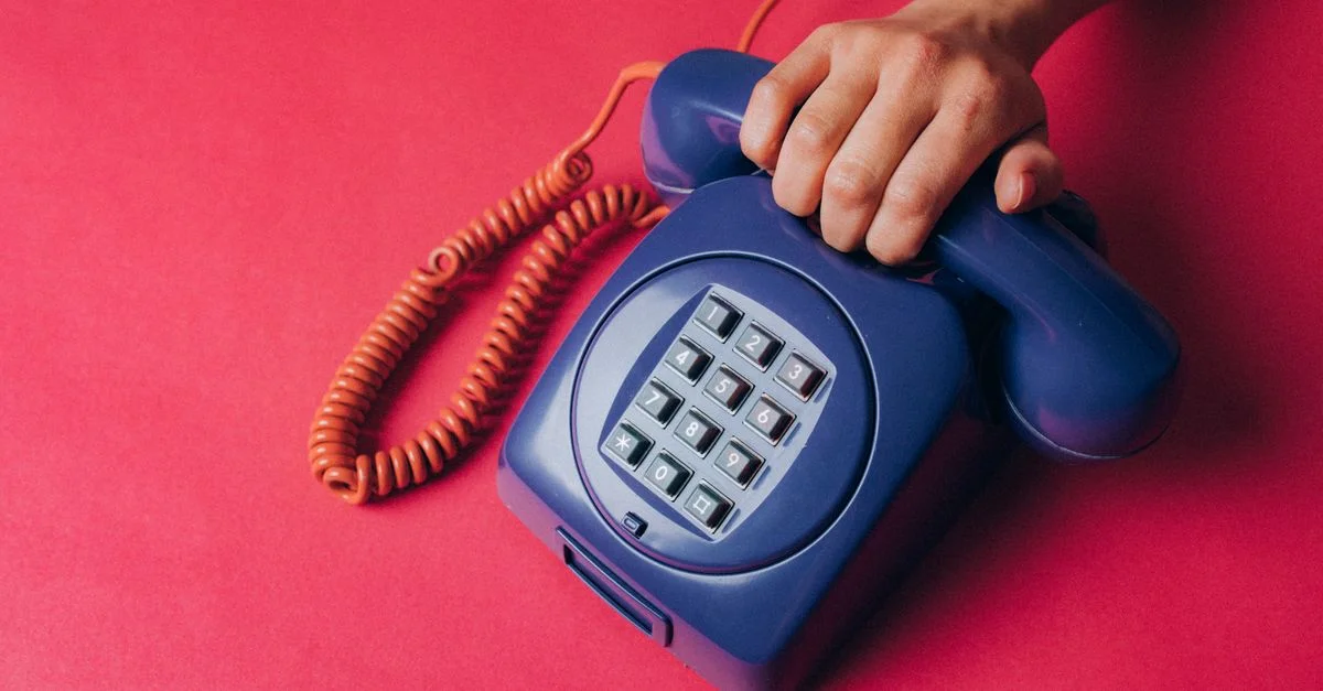 Gros plan sur une main tenant un téléphone vintage bleu, évoquant la nostalgie et les vibes rétro.