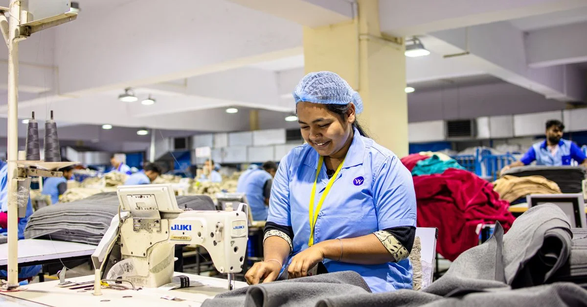 Une femme ouvrière textile utilise une machine à coudre dans un environnement d'usine animé.