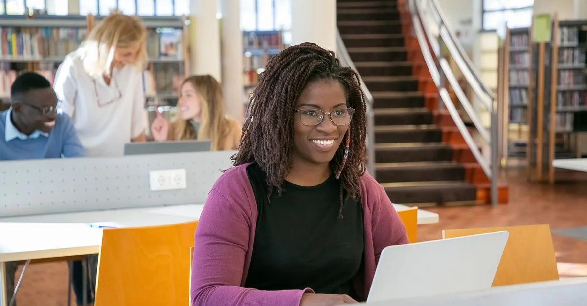Un groupe divers d'étudiants étudiant dans une bibliothèque, engagés avec des ordinateurs portables et des livres, promouvant l'éducation et le travail d'équipe.