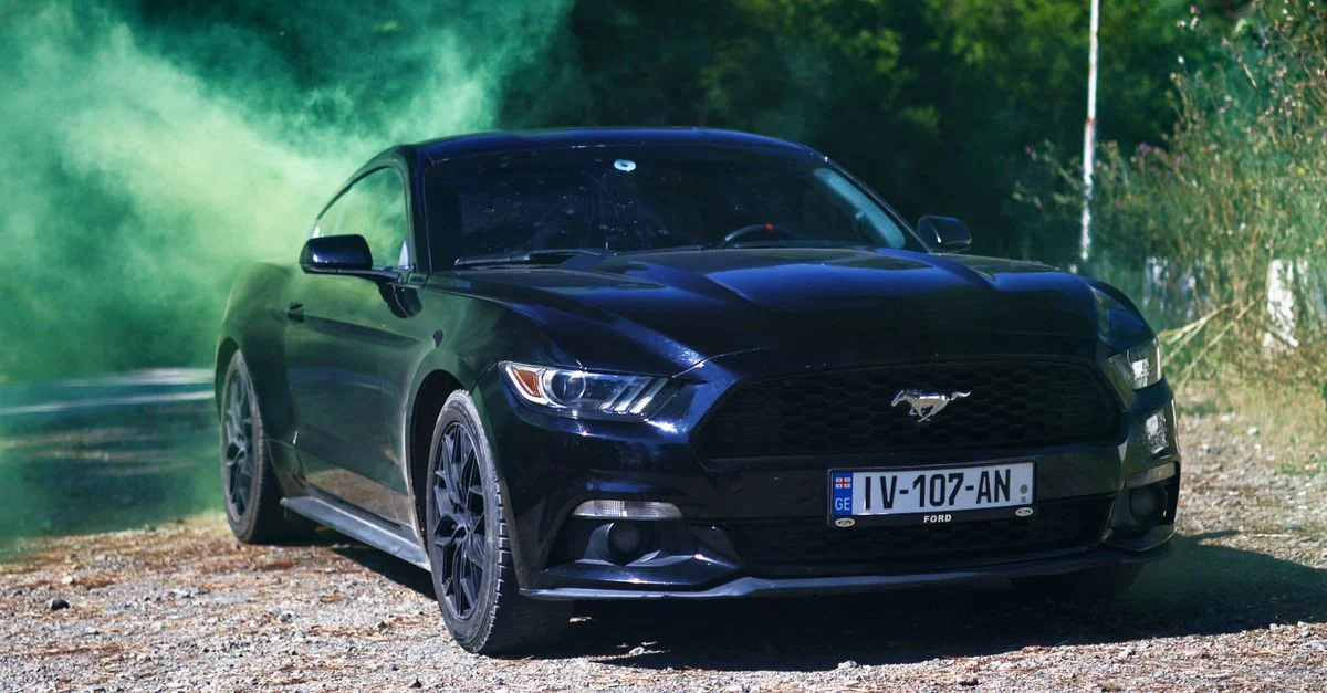 Une élégante voiture de sport noire, enveloppée de fumée verte, garée en plein air par une journée ensoleillée.