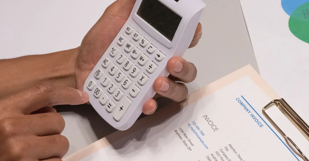 Gros plan sur des mains utilisant une calculatrice à côté d'une facture d'entreprise, illustrant un concept de calcul financier.