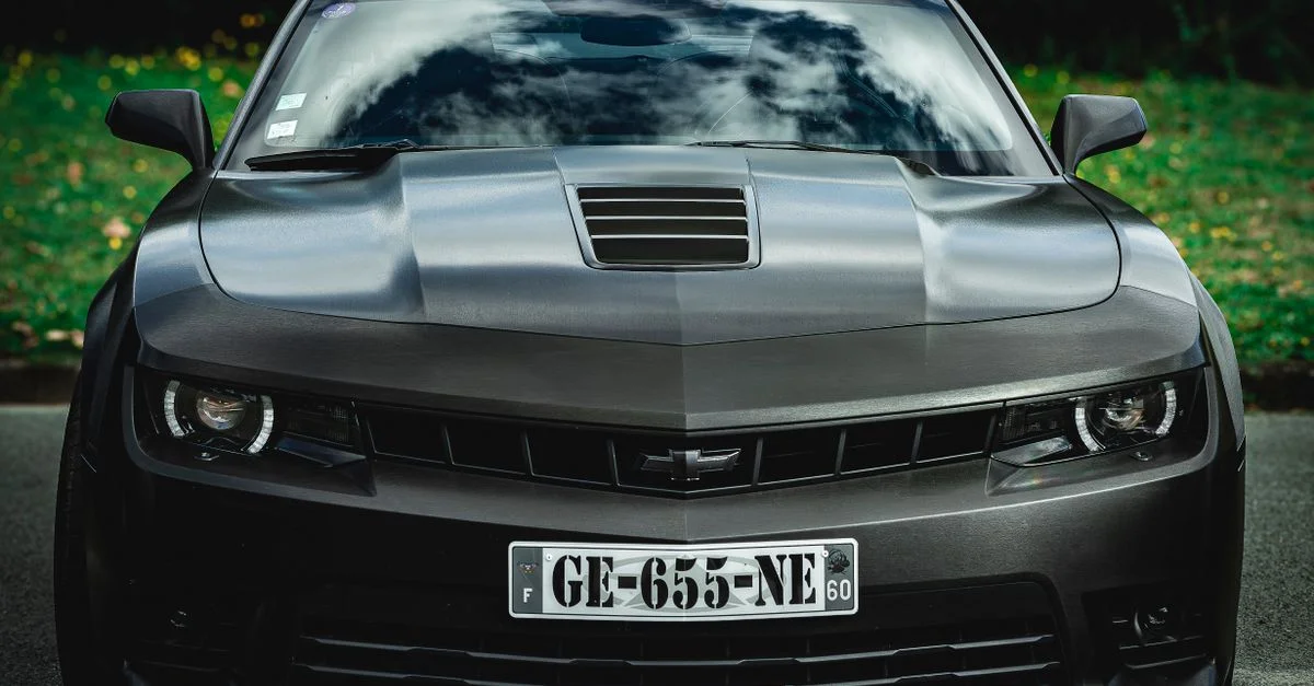 Vue de face en gros plan d'une voiture de sport noire élégante avec une plaque d'immatriculation, garée en plein air.