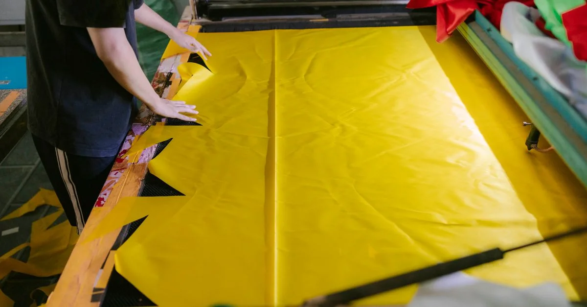 Une personne coupe du tissu jaune pour la production textile dans un atelier.