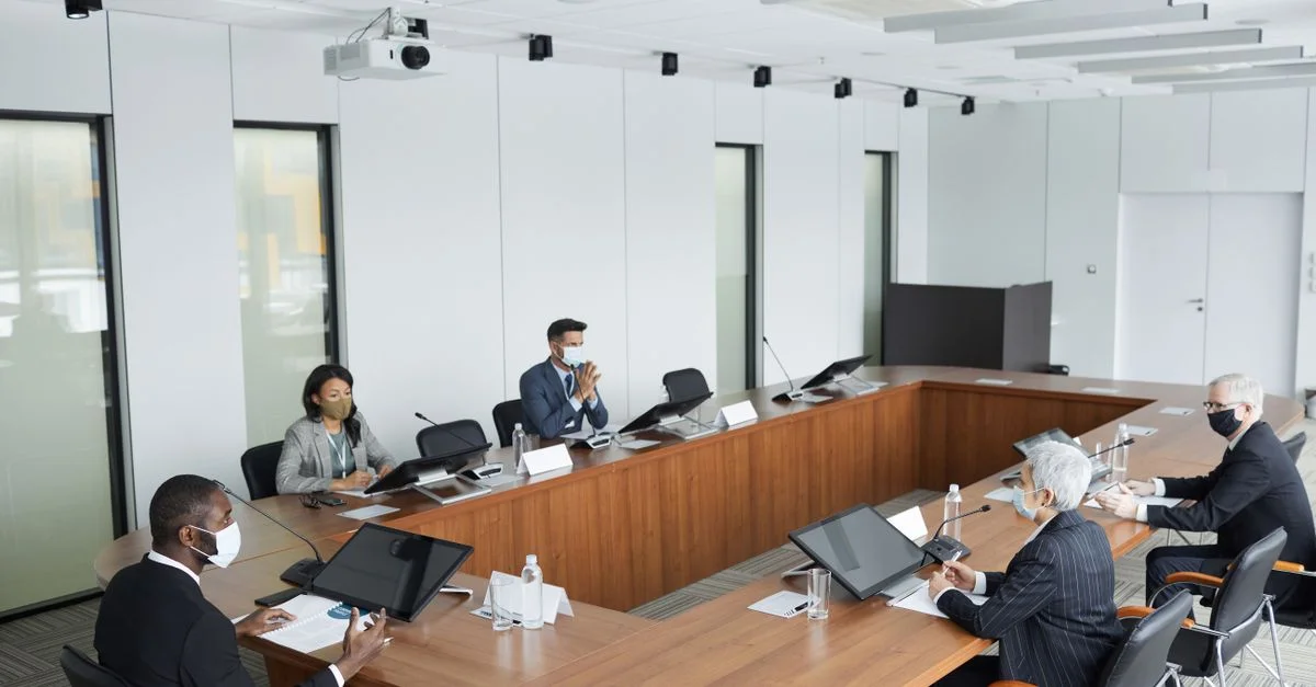 Professionnels en affaires portant des masques participant à une réunion de conférence dans un cadre moderne.