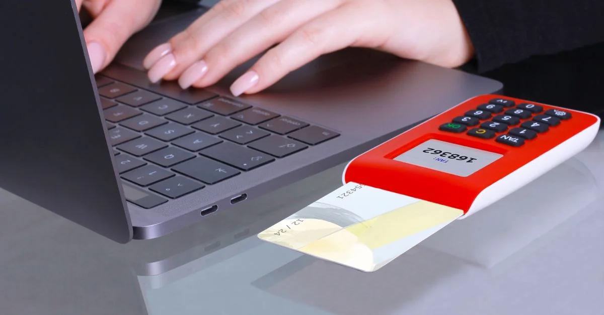 Gros plan sur des mains utilisant un ordinateur portable et un lecteur de carte pour un paiement en ligne.