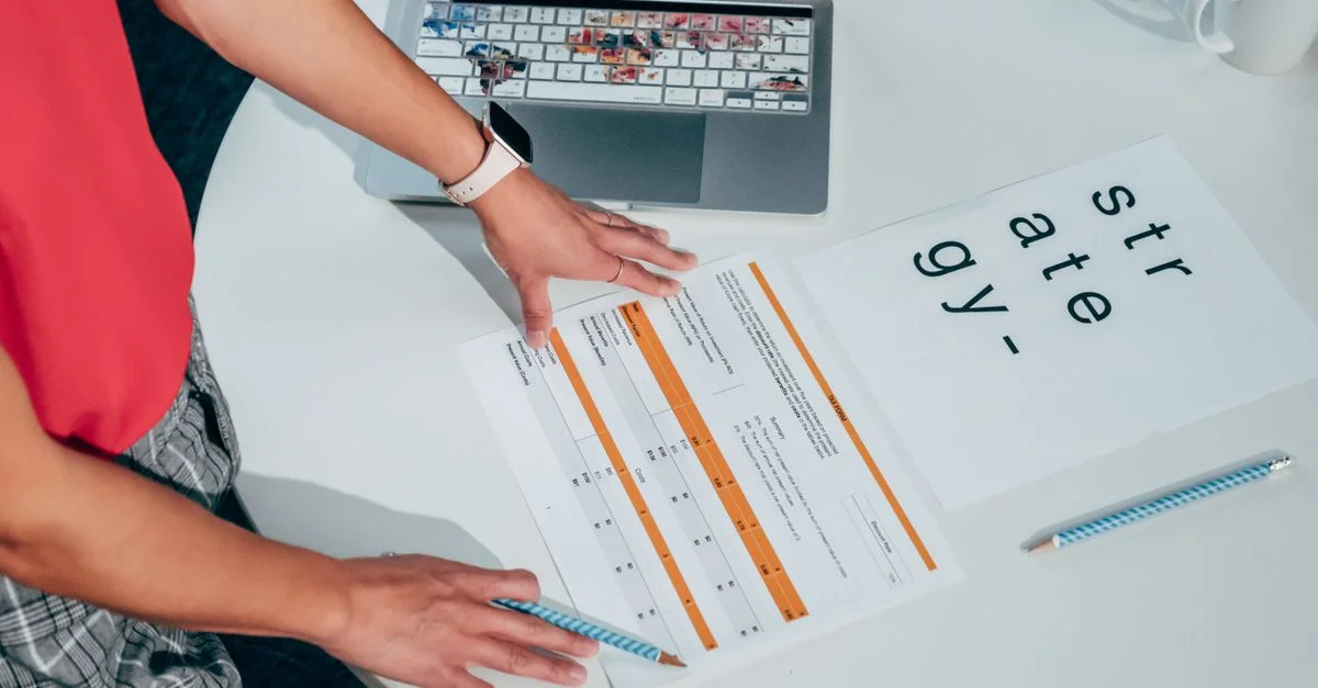 Vue aérienne d'une personne élaborant une stratégie avec des documents et un ordinateur portable sur une table.