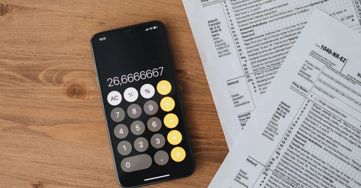 Vue de dessus d'une calculatrice smartphone et de formulaires fiscaux sur une table en bois.