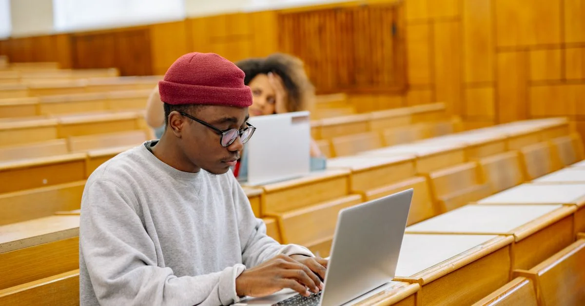 Des étudiants se concentrent sur des ordinateurs portables dans un vaste amphithéâtre universitaire, apprenant et travaillant numériquement.