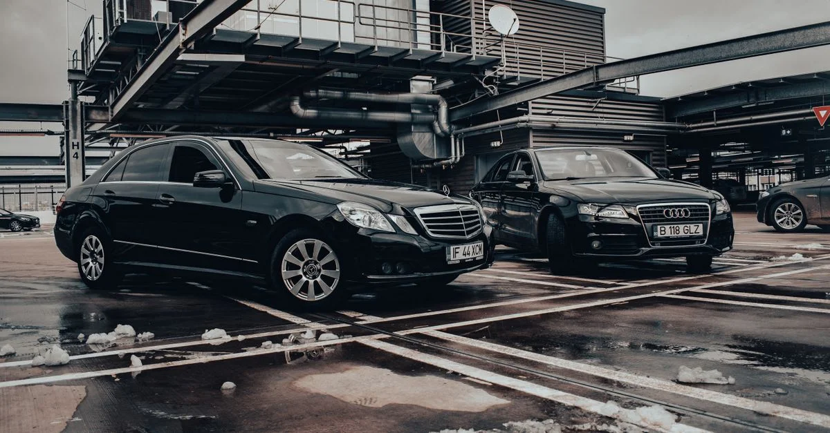 Deux voitures de luxe noires garées dans un cadre industriel hivernal, mettant en avant l'élégance et le design moderne.
