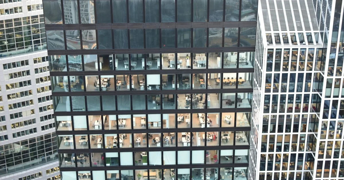 Façade d'un immeuble de grande hauteur avec des intérieurs de bureau visibles, mettant en valeur l'architecture urbaine.